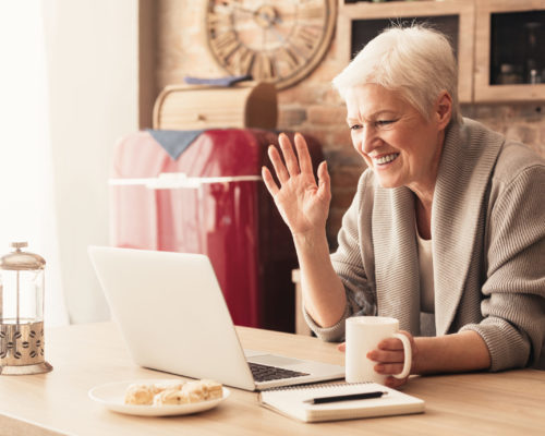 Elderly woman making video call on laptop in kitchen Elderly woman making video call on laptop in kitchen, waving at screen, chatting with children, free space